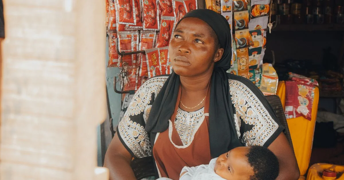 Une femme tient son bébé dans un stand de marché coloré entouré de marchandises.