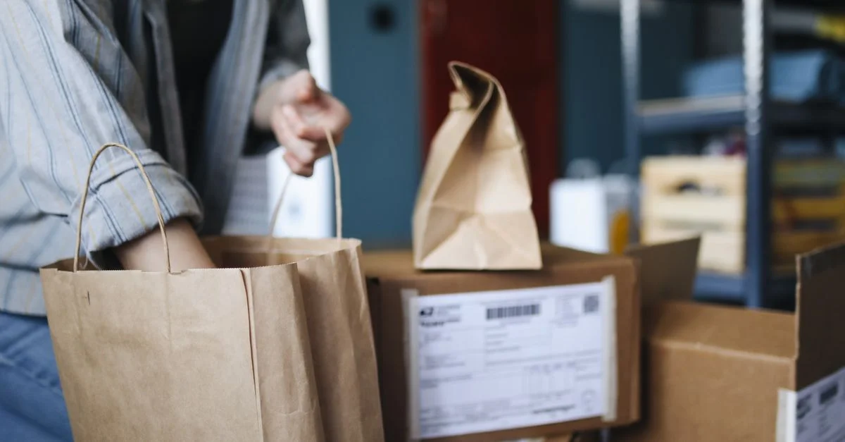 Femme triant des colis et des sacs en papier dans un cadre domestique, mettant en avant les achats en ligne et la livraison.