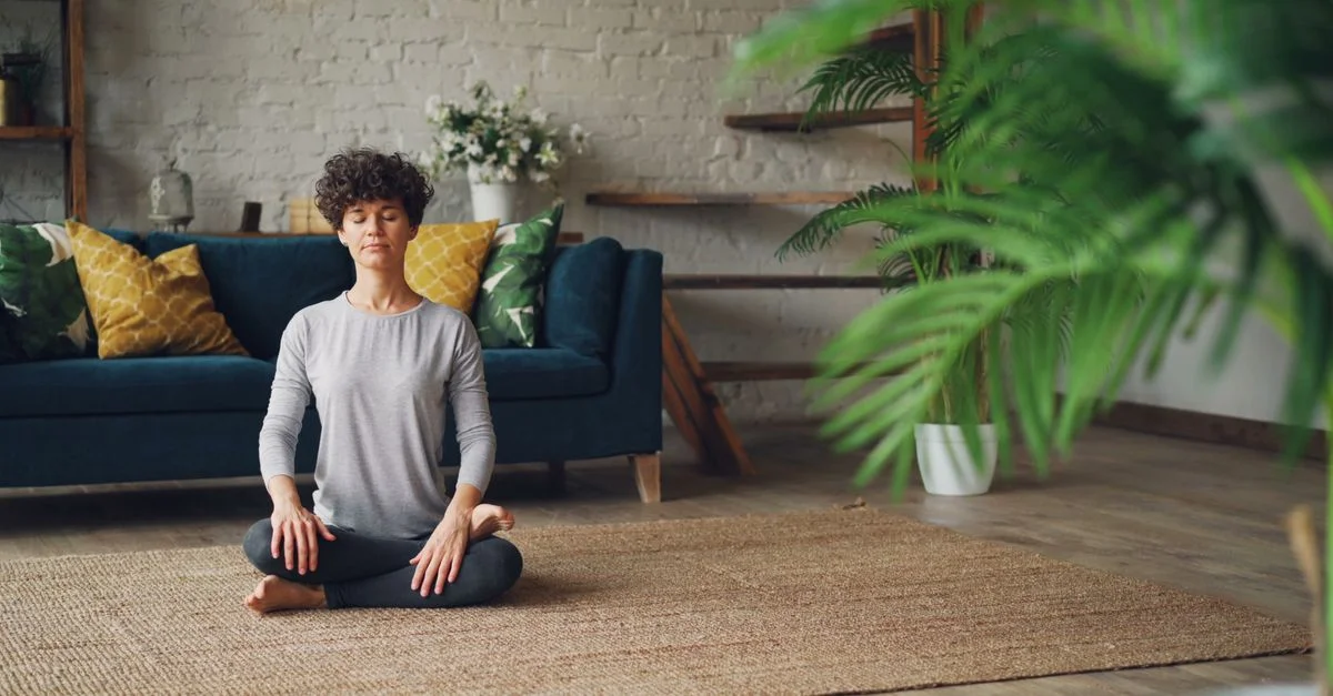 Femme en méditation dans un salon confortable avec une décoration naturelle, favorisant la relaxation.
